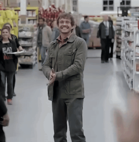 A Man In A Green Jacket Is Smiling In A Grocery Store While Holding A Knife GIF