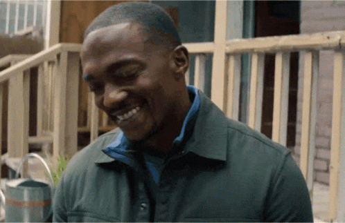 A Man In A Green Jacket Is Smiling In Front Of A Railing GIF