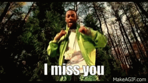 A Man In A Green Jacket Is Standing In The Woods With The Words `` I Miss You '' Written On The Screen . GIF