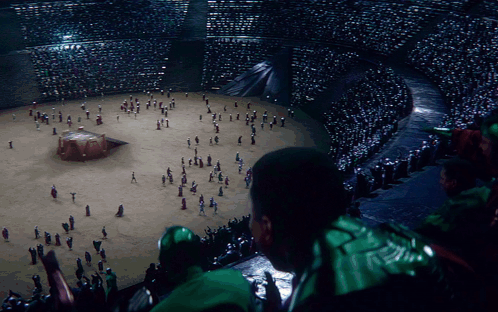 A Man In A Green Jacket Looks At A Crowd Of People GIF