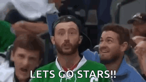A Man In A Green Jersey Is Sitting In A Crowd Of People Watching A Hockey Game And Says `` Lets Go Stars '' . GIF