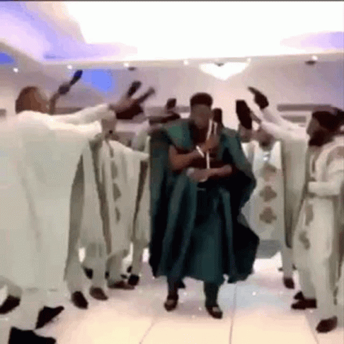 A Man In A Green Robe Is Dancing With A Group Of Men In White Robes . GIF
