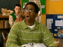 A Man In A Green Shirt And Glasses Is Sitting At A Desk In A Classroom With His Mouth Open . GIF