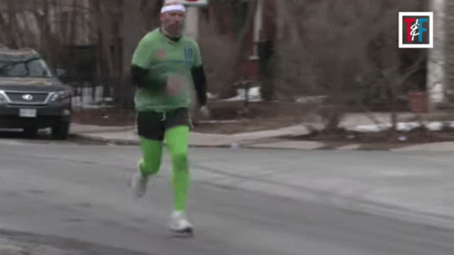 A Man In A Green Shirt And Green Pants Is Running Down A Street GIF