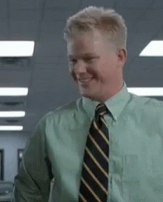 A Man In A Green Shirt And Tie Is Smiling And Looking At The Camera . GIF