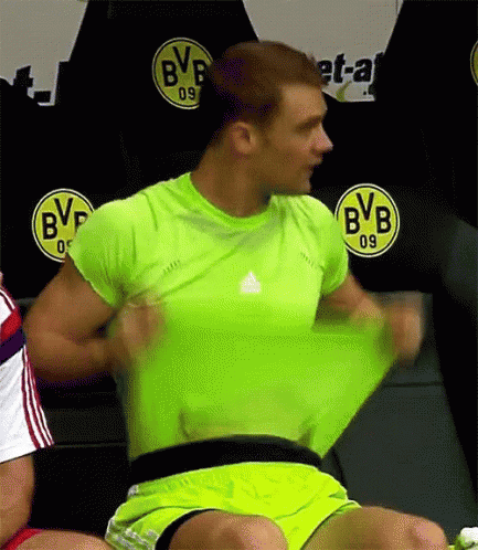 a man in a green shirt and yellow shorts is taking off his shirt in front of a bvb logo .