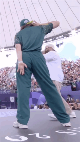 A Man In A Green Shirt Is Dancing In Front Of A Crowd With The Number 2 On The Floor GIF