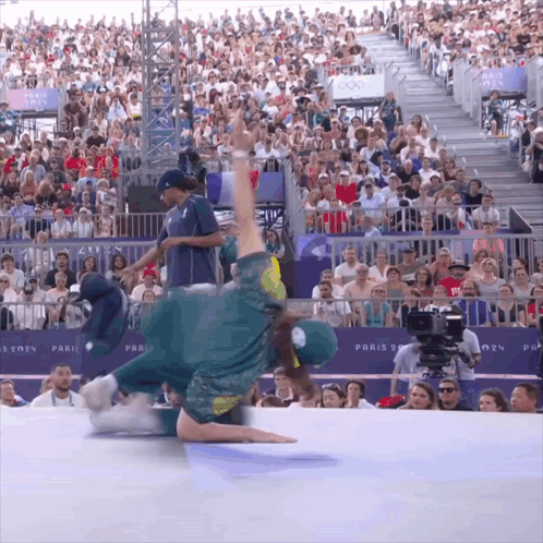 A Man In A Green Shirt Is Doing A Trick In Front Of A Crowd With A Paris Sign Behind Him GIF
