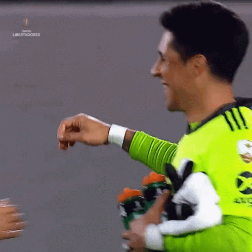 A Man In A Green Shirt Is Giving A Fist Bump To Another Man GIF