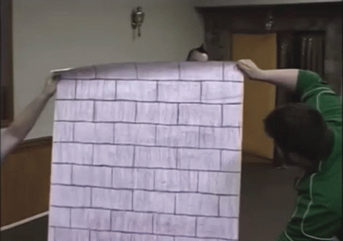 A Man In A Green Shirt Is Holding A Large Piece Of Paper With A Brick Pattern On It GIF