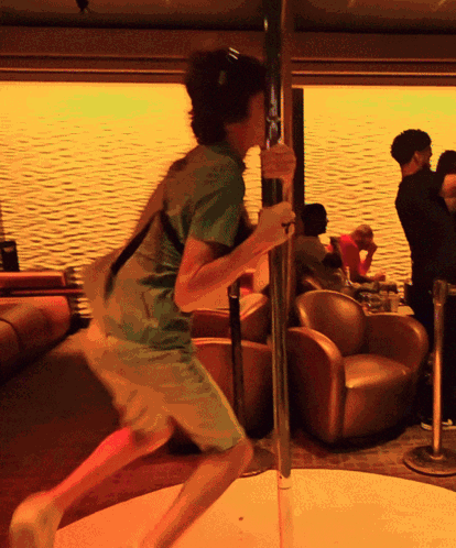 A Man In A Green Shirt Is Holding A Pole In A Room GIF
