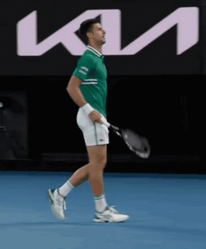 A Man In A Green Shirt Is Holding A Tennis Racquet In Front Of A Kia Sign GIF