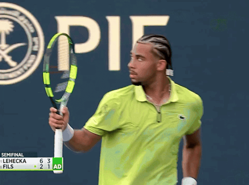 a man in a green shirt is holding a tennis racquet in front of a sign that says " it "