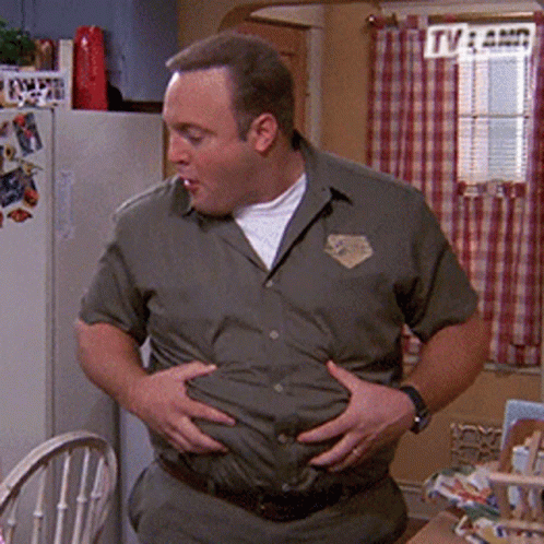A Man In A Green Shirt Is Holding His Belly In A Kitchen . GIF