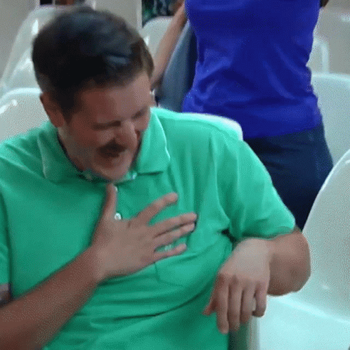 A Man In A Green Shirt Is Holding His Chest And Smiling GIF