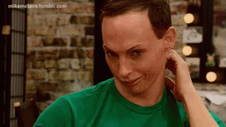 A Man In A Green Shirt Is Holding His Hand To His Ear And Making A Funny Face . GIF