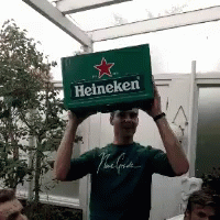 A Man In A Green Shirt Is Holding Up A Box Of Heineken GIF
