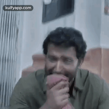 A Man In A Green Shirt Is Laughing While Holding A Pink Object In His Hand . GIF