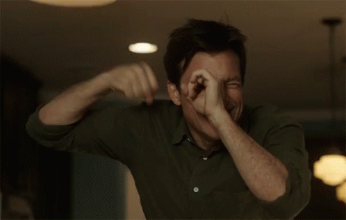A Man In A Green Shirt Is Making A Funny Face And Covering His Mouth With His Hands . GIF