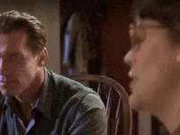 A Man In A Green Shirt Is Sitting In A Chair Looking At Another Man . GIF