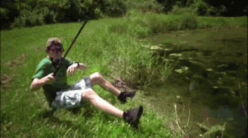 A Man In A Green Shirt Is Sitting In The Grass Holding A Fishing Rod GIF