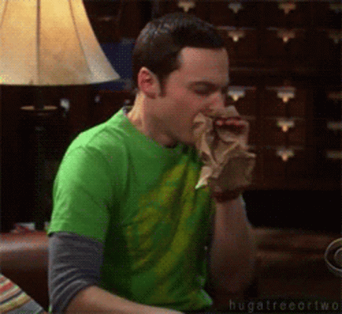 A Man In A Green Shirt Is Sitting On A Couch Eating Something GIF