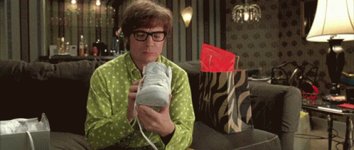 A Man In A Green Shirt Is Sitting On A Couch Holding A Shoe GIF