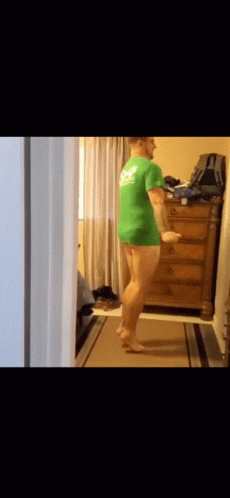 A Man In A Green Shirt Is Standing In A Hallway . GIF