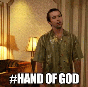A Man In A Green Shirt Is Standing In A Living Room With The Words Hand Of God Written On The Screen . GIF