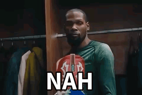 A Man In A Green Shirt Is Standing In A Locker Room With Clothes Hanging On The Racks And Says Nah . GIF