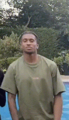 A Man In A Green Shirt Is Standing In Front Of A Swimming Pool GIF