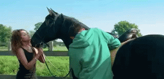 A Man In A Green Shirt Is Standing Next To A Woman Holding A Black Horse GIF