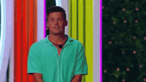 A Man In A Green Shirt Is Standing On A Stage In Front Of A Colorful Background . GIF
