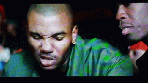 A Man In A Green Shirt Is Talking To Another Man In A Dark Room GIF