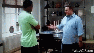 A Man In A Green Shirt Is Talking To Another Man In A Living Room . GIF