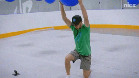 A Man In A Green Shirt Is Throwing A Blue Ball On A Rink With Nick Written On The Wall Behind Him GIF
