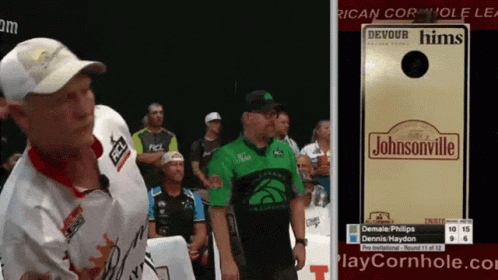 A Man In A Green Shirt Stands Next To A Sign That Says Johnsonville GIF