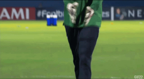 A Man In A Green Shirt Stands On A Soccer Field In Front Of An Ami Banner GIF