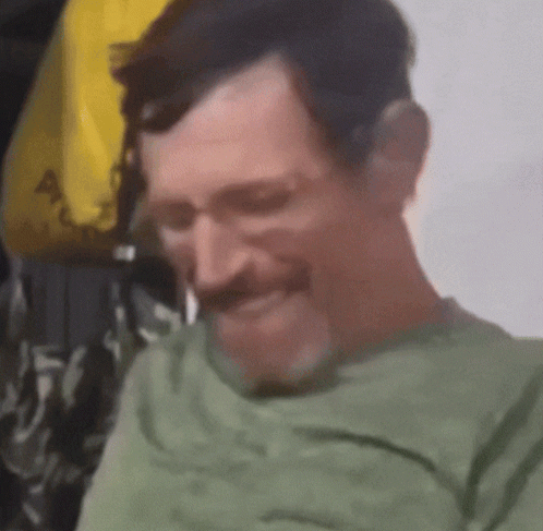 A Man In A Green Shirt With A Mustache Is Smiling GIF