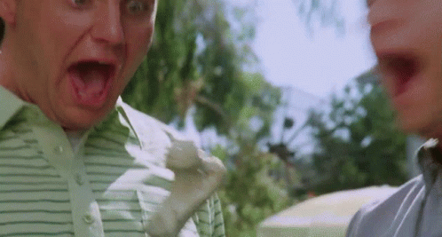 A Man In A Green Striped Shirt Is Making A Funny Face While Another Man Looks On . GIF