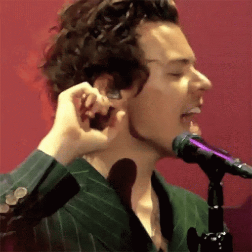 A Man In A Green Suit Is Singing Into A Microphone While Holding His Ear . GIF