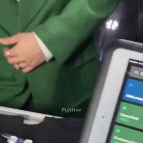 A Man In A Green Suit Is Standing Next To A Tablet With The Word Fugitive On The Bottom GIF