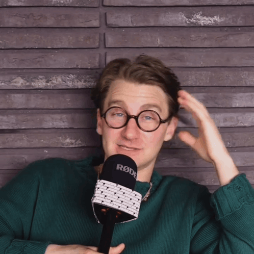 A Man In A Green Sweater Holds A Rode Microphone GIF