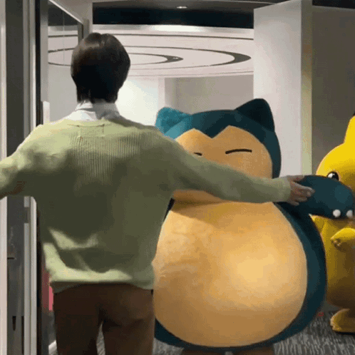 A Man In A Green Sweater Is Hugging A Stuffed Animal That Looks Like Snorlax GIF