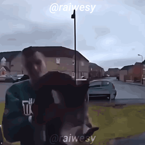 a man in a green sweatshirt is standing in front of a street with the name @raiwesy on the bottom