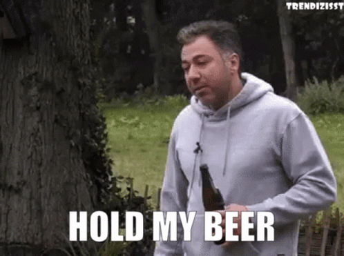 A Man In A Grey Hoodie Is Holding A Bottle Of Beer And Saying Hold My Beer GIF