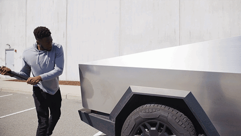 A Man In A Grey Hoodie Is Pushing A Silver Truck GIF