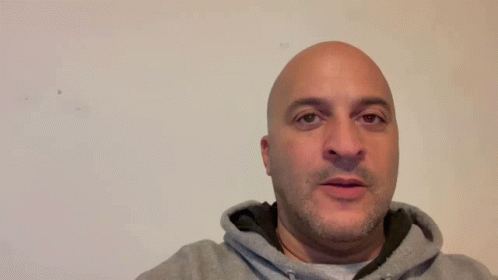 A Man In A Grey Hoodie Is Standing In Front Of A Sign That Says Thank You GIF