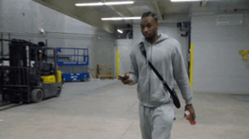A Man In A Grey Hoodie Is Walking In A Warehouse GIF