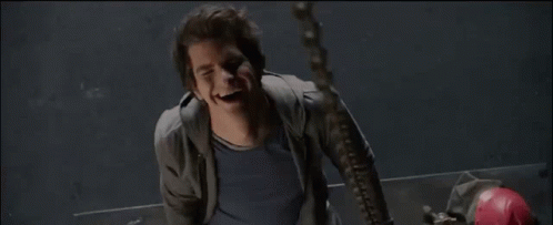 A Man In A Grey Jacket And Blue Shirt Smiles While Hanging From A Chain GIF